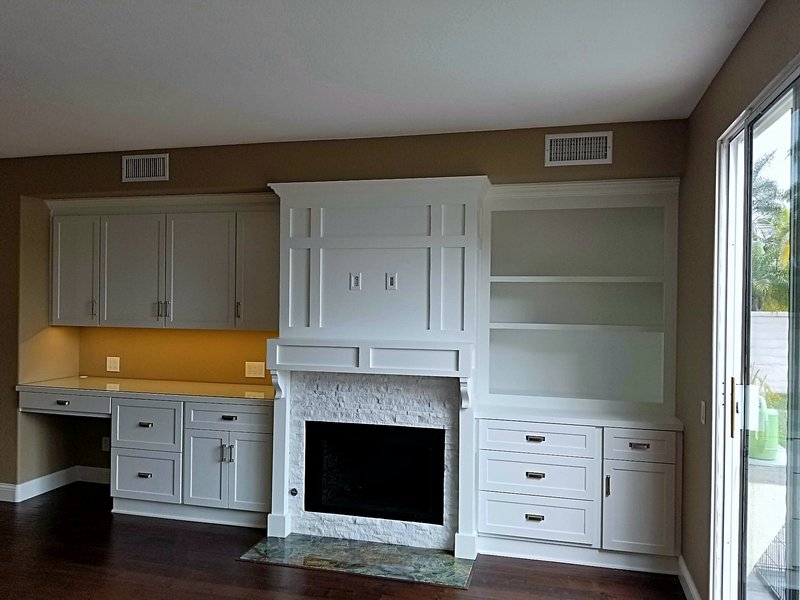 Living room wall with a stacked-stone fireplace, white built-in cabinets and open shelving, and a built-in desk with under-cabinet lighting