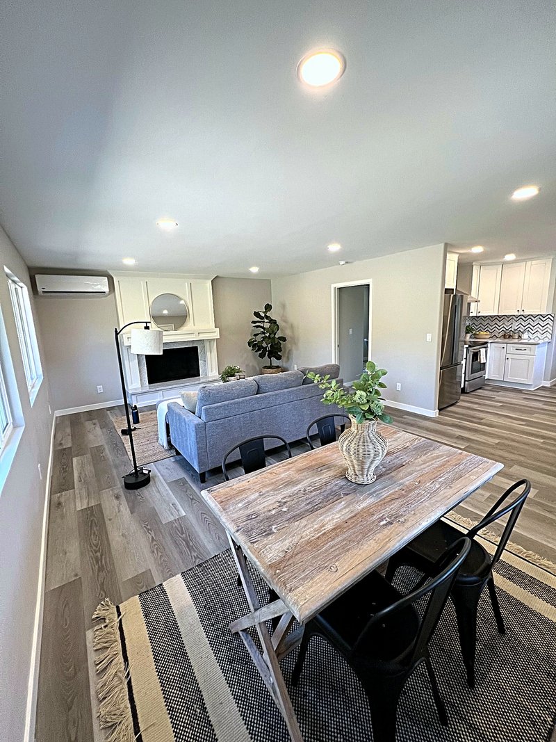 Open living and dining room with luxury vinyl plank floors, recessed lighting, a paneled fireplace wall, and the white shaker kitchen visible beyond