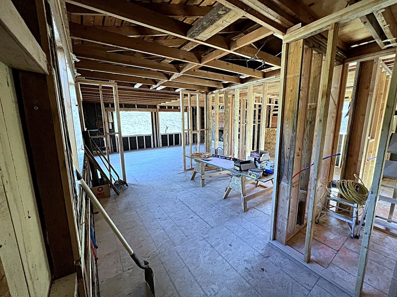 Second view of the same gut renovation at framing: newly framed interior walls and door openings, exposed ceiling joists, and rough plumbing runs in the walls