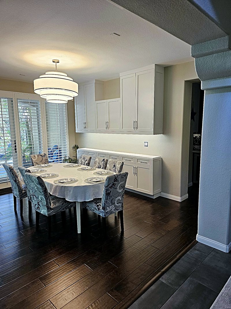 The finished dining room with the painted white built-in buffet and wall cabinets, set table, and dark hardwood floors