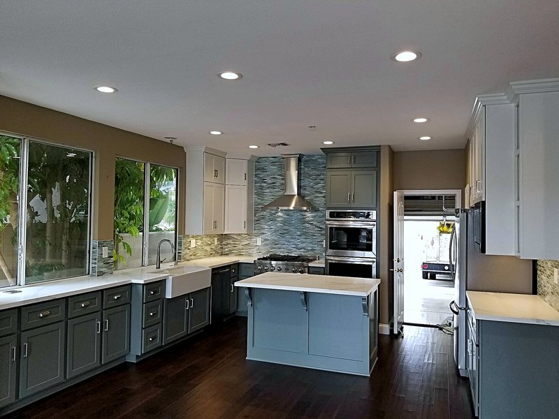Kitchen remodel with blue-gray shaker cabinets, a center island, farmhouse sink, mosaic tile backsplash, professional range with stainless hood, and double wall ovens