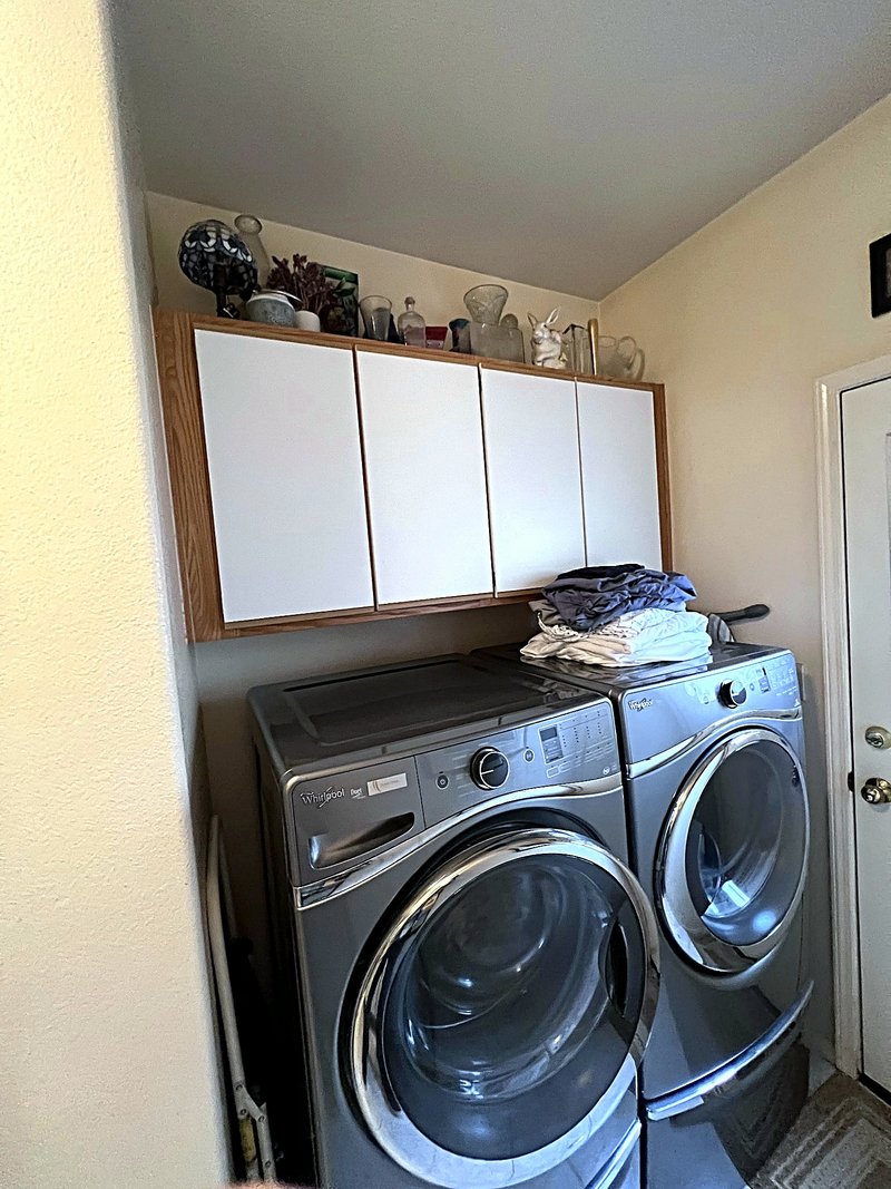 Laundry room with a front-load washer and dryer pair and white overhead storage cabinets with oak trim