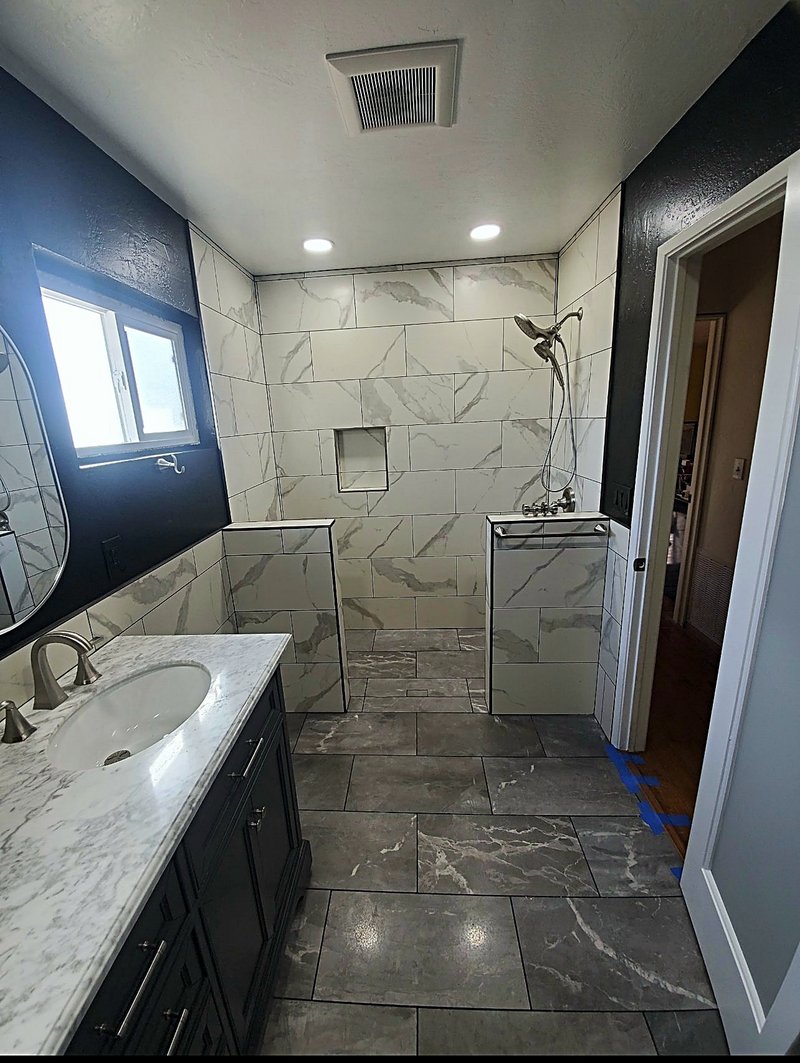 Bathroom remodel with a dark vanity and marble-look countertop, plus an open walk-in shower in large marble-look tile with a recessed niche and gray stone-look floor tile