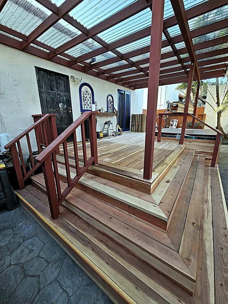 Wide tiered steps up to the new wood deck, with rust-red painted pergola posts and railings