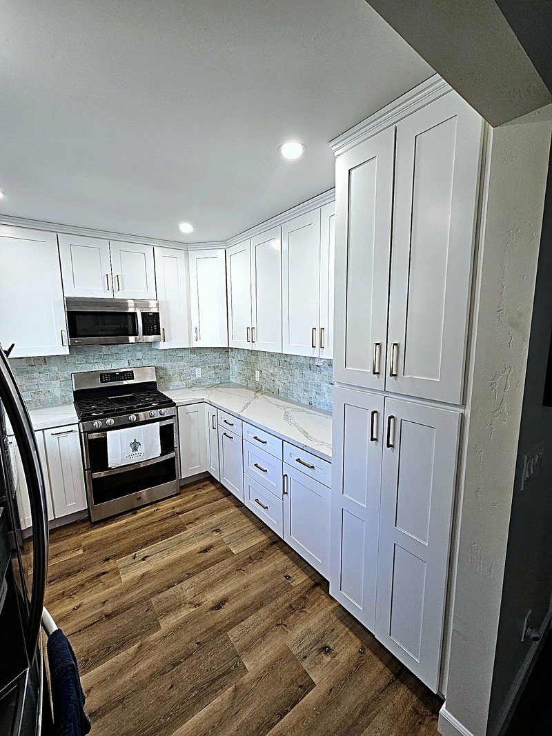 Another angle of the same kitchen: floor-to-ceiling white pantry cabinets with brass pulls, quartz countertops, and the sea-glass tile backsplash