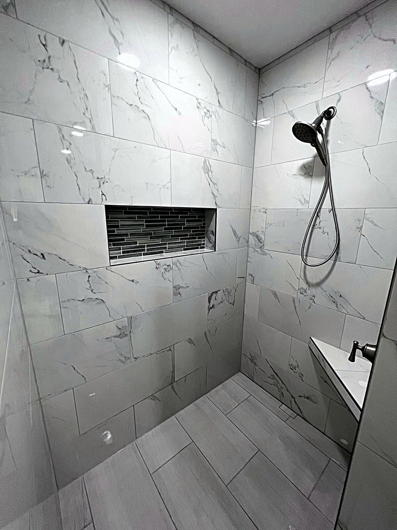 Walk-in shower in marble-look porcelain tile with a wide mosaic-tile niche, floating corner seat, handheld shower, and linear drain