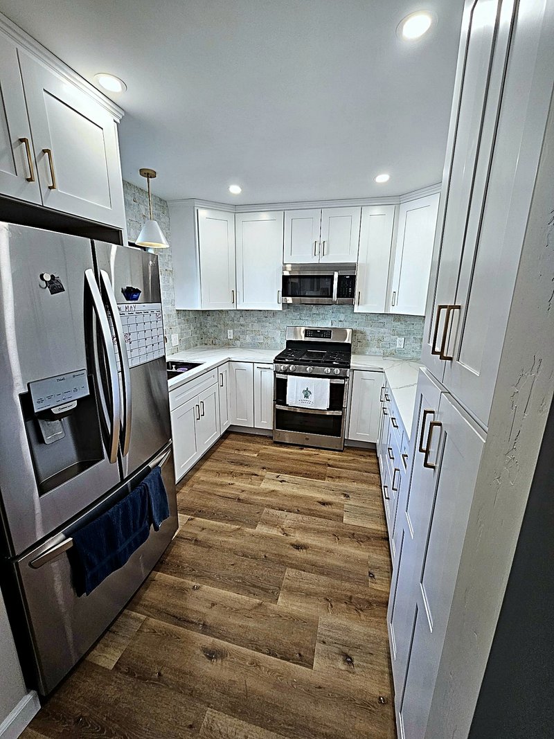 White shaker kitchen with a sea-glass subway tile backsplash, brass cabinet pulls, stainless French-door refrigerator, and gas range
