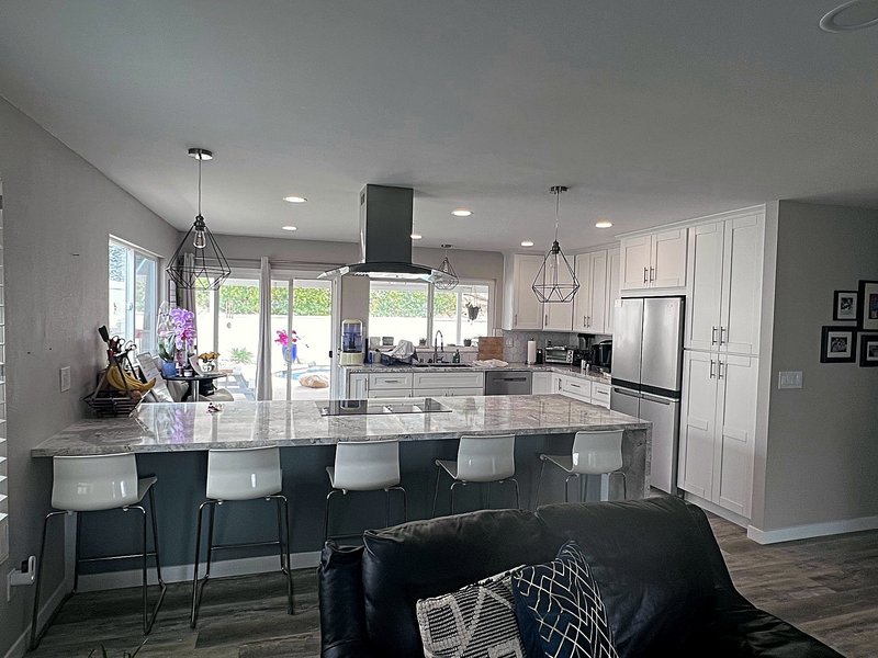 White shaker kitchen with a marble-look waterfall island, glass cooktop, stainless island range hood, geometric pendant lights, and bar seating