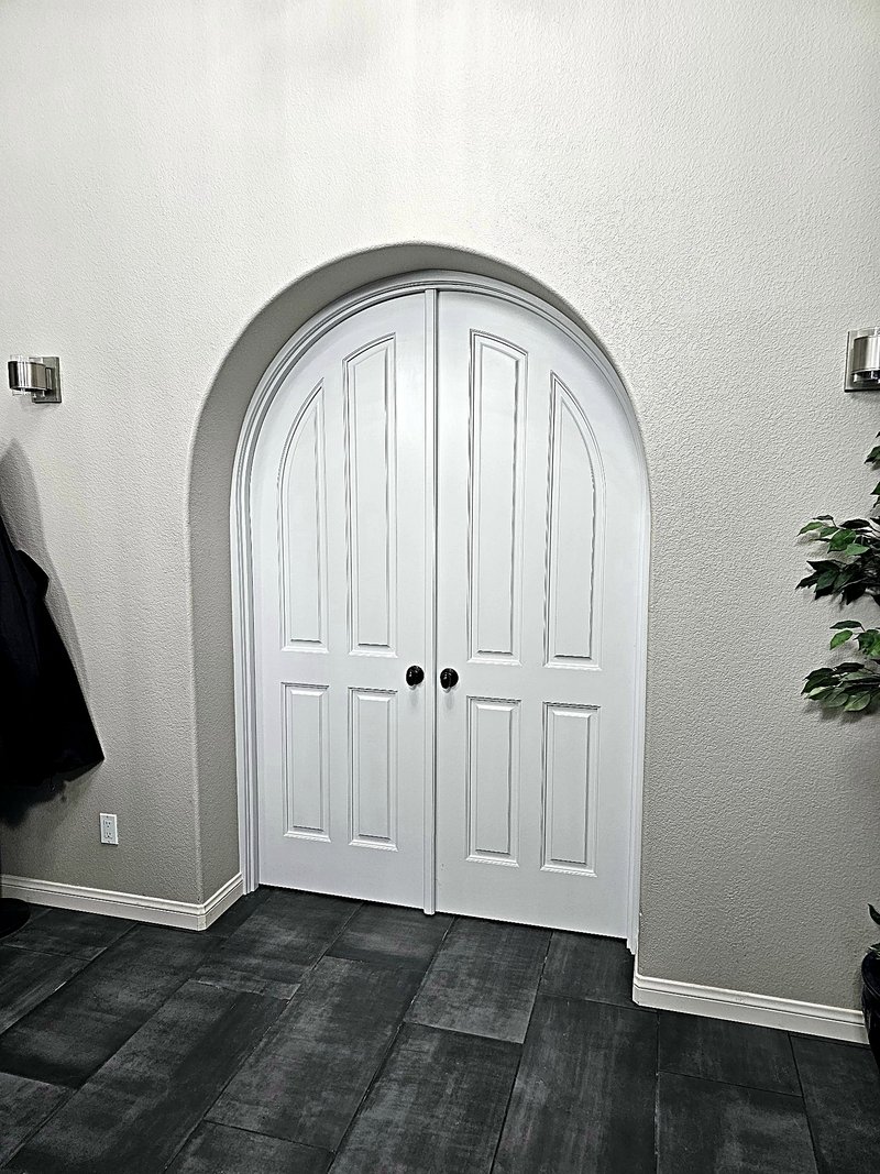 The same arched double doors finished in white paint with black knobs, in the arched entry with dark tile floors