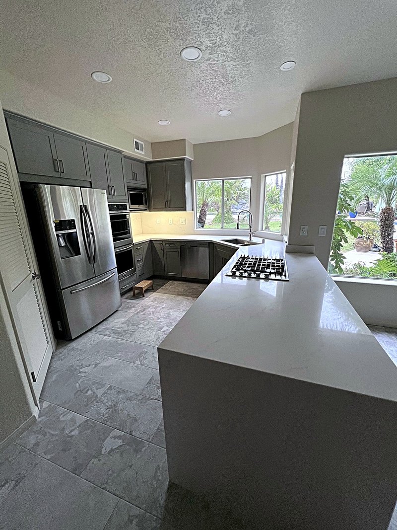 Kitchen remodel with gray shaker cabinets, white quartz counters, a peninsula with a gas cooktop and waterfall end, double wall ovens, and stone-look tile flooring