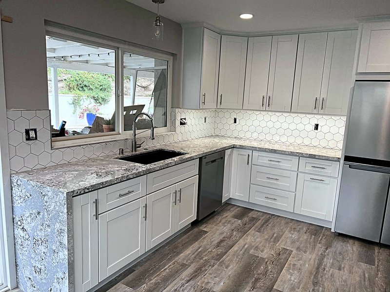 White shaker kitchen with a white hexagon tile backsplash, granite countertops with a waterfall end, undermount sink, and luxury vinyl plank floors