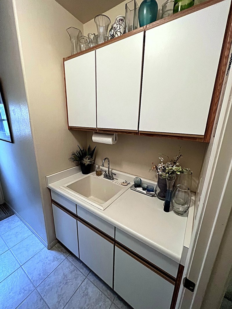 Second view of the laundry room: a drop-in utility sink set in a white countertop with base and overhead storage cabinets