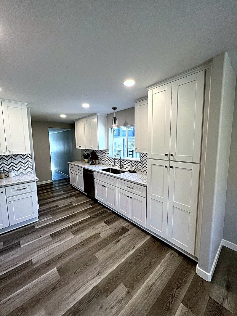 White shaker kitchen with a black-and-white chevron marble backsplash, built-in pantry cabinets, quartz countertops, and luxury vinyl plank floors