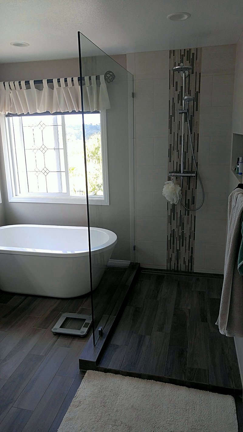 Primary bathroom with a freestanding oval soaker tub beside a glass-panel walk-in shower with a vertical mosaic accent stripe and wood-look tile floors