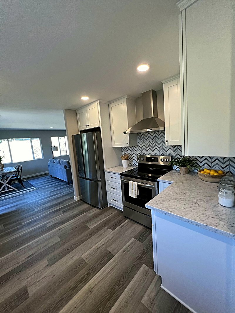 White shaker kitchen with a stainless range and chimney hood over a black-and-white chevron marble backsplash, quartz counters, and the open living room beyond
