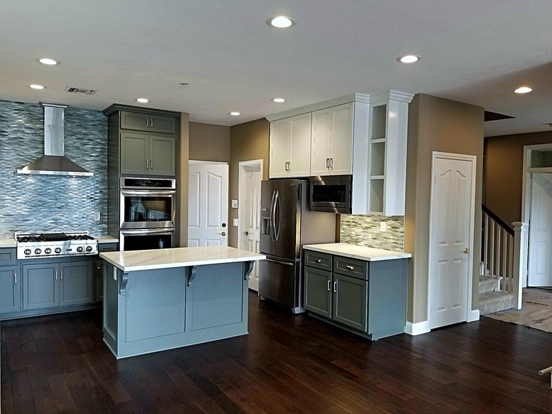 Second view of the blue-gray shaker kitchen: center island, built-in double ovens, professional range with stainless hood, and mosaic tile backsplash