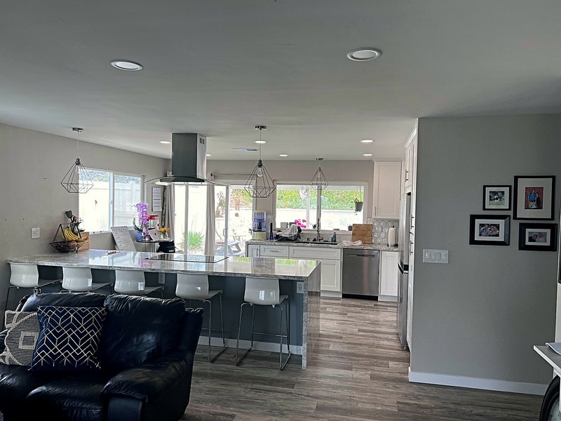 Second view of the white shaker kitchen: the waterfall island from the living room, tall pantry cabinets, French-door refrigerator, and hexagon tile backsplash at the sink