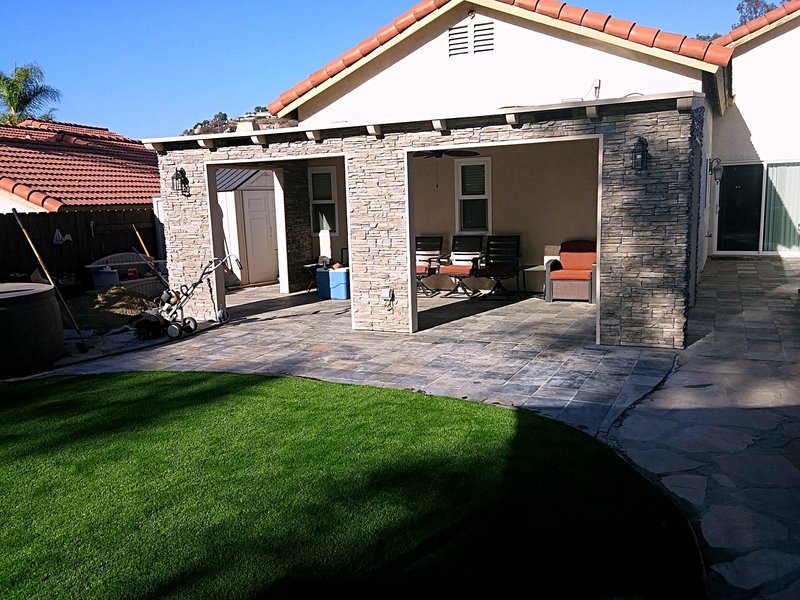 Backyard patio we built with a stone-clad covered patio, slate tile flooring, and a new artificial turf lawn