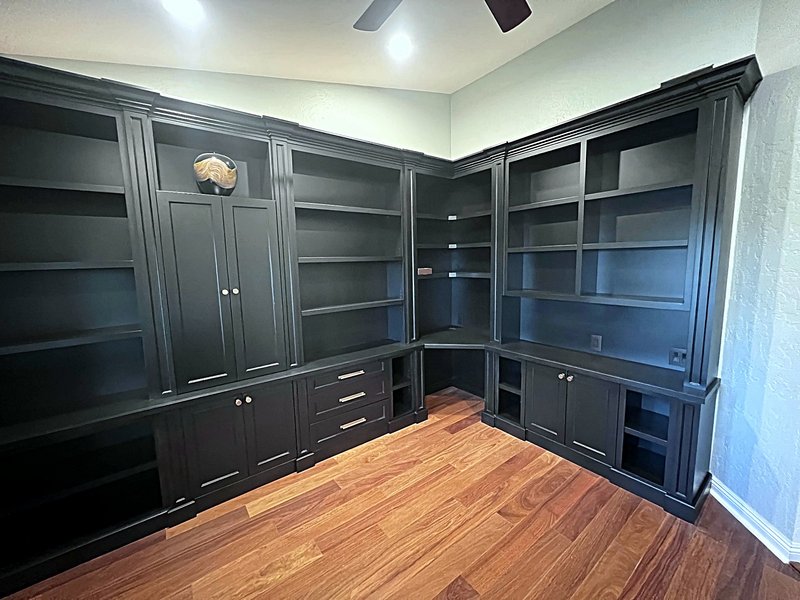 Second view of the home office: black built-in shelving wrapping the corner with a corner desk, drawer banks with brass pulls, and closed storage cabinets