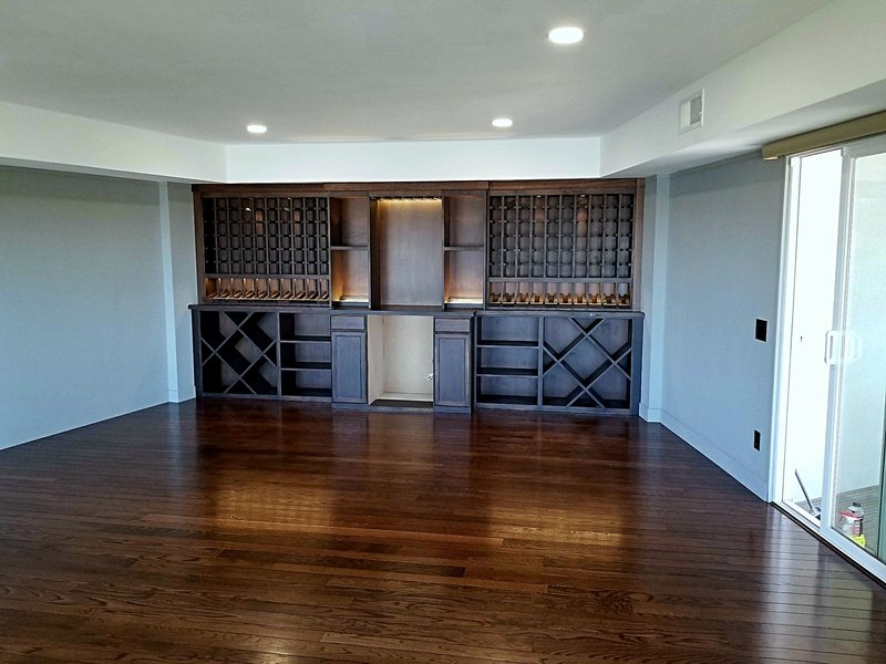 Dark wood built-in wine bar we built with lattice bottle racks, glass holders, X-shelf storage, and accent lighting over hardwood floors