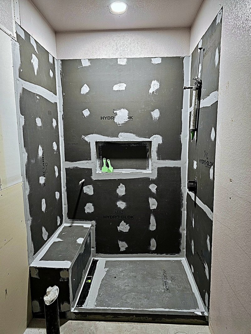 Walk-in shower at the waterproofing stage: waterproof backer board with sealed seams and fasteners, a framed niche, built-in bench, and linear drain, ready for tile