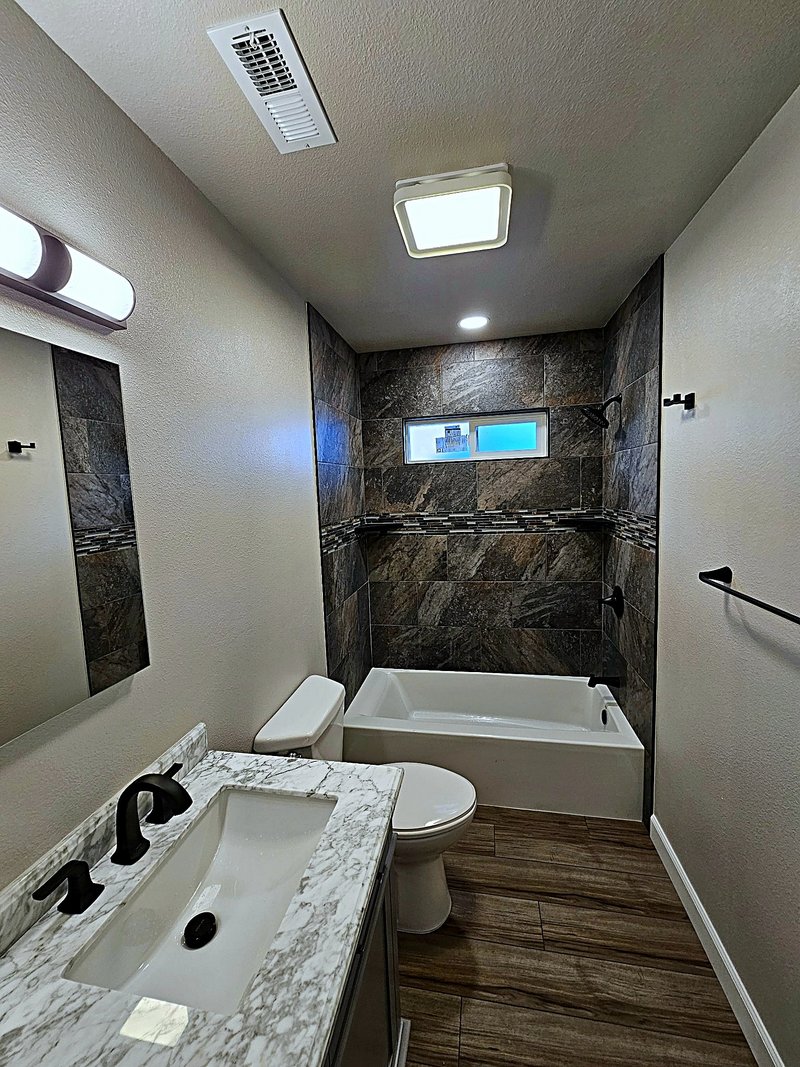 Hall bathroom remodel with a new alcove tub, stone-look tile surround with a mosaic accent strip, matte black fixtures, and wood-look plank flooring