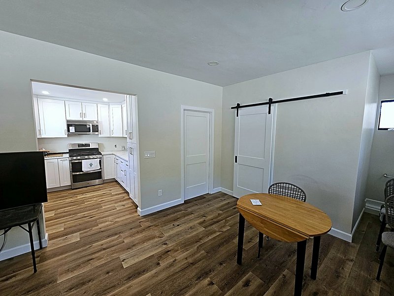 View from the dining room into the white shaker kitchen, with wood-look plank floors, a white sliding barn door, and stainless appliances