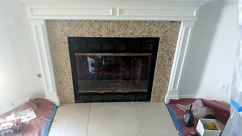 Fireplace remodel just finished: a stacked-stone surround with a white painted mantel and new large-format tile hearth, with floor protection still down