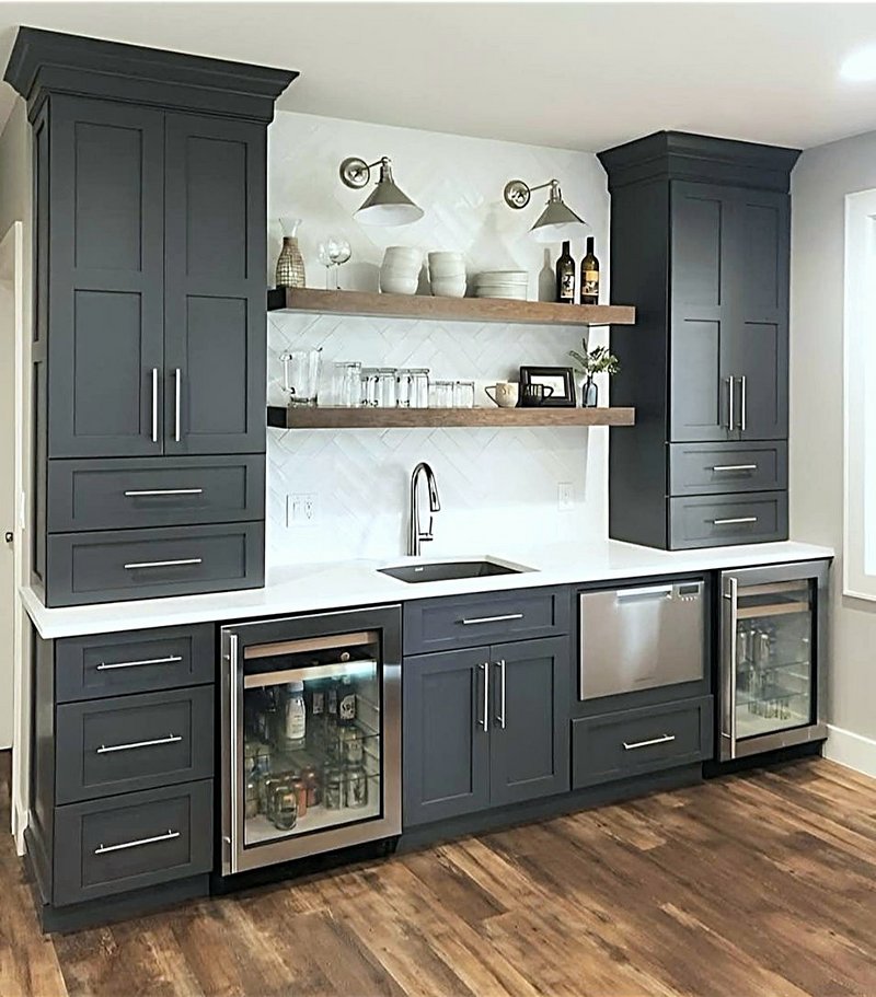 Navy wet bar and beverage center we built with two glass-front beverage fridges, a bar sink, floating wood shelves, herringbone tile backsplash, and tall storage cabinets