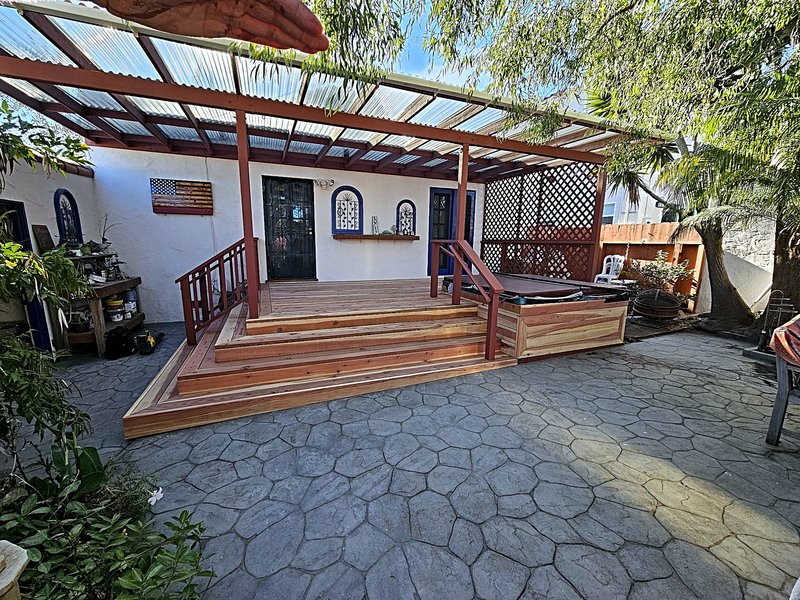 Wide view of the deck, covered pergola, and hot tub from the stone-paved backyard